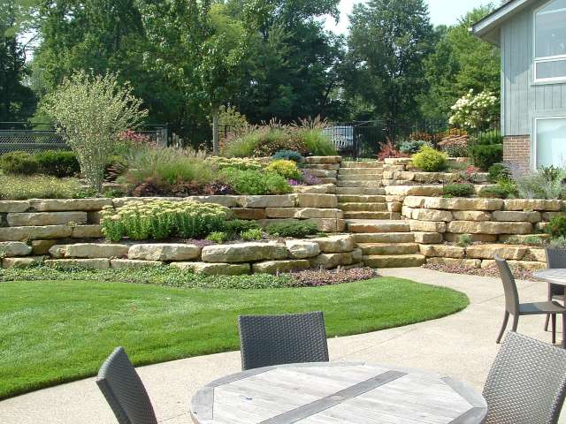 Hillside and natural stone walls above a patio and lawn area, beautifully landscaped with an assortment of plant life.